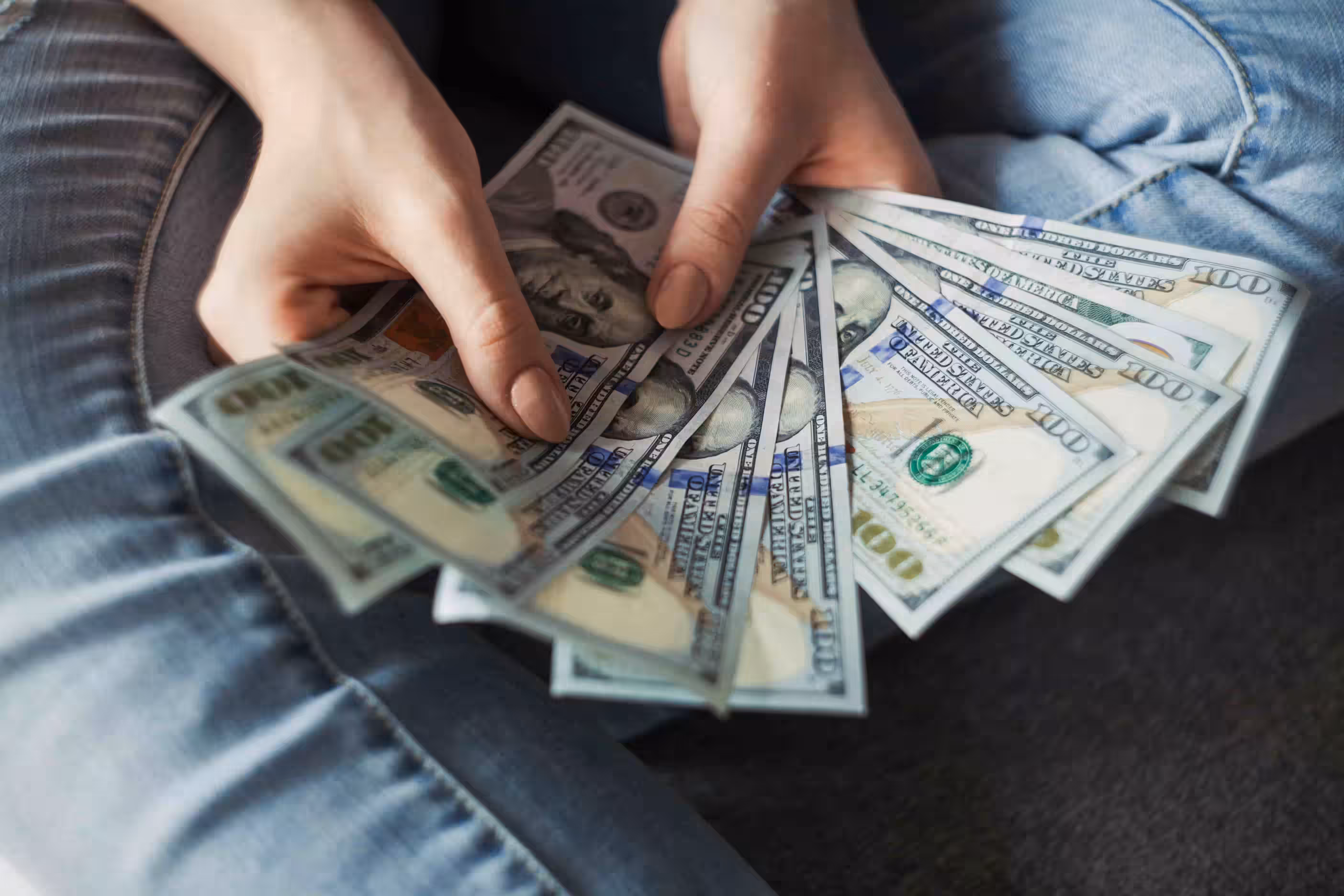 person sitting on floor with hundred-dollar bills splayed out in their hands